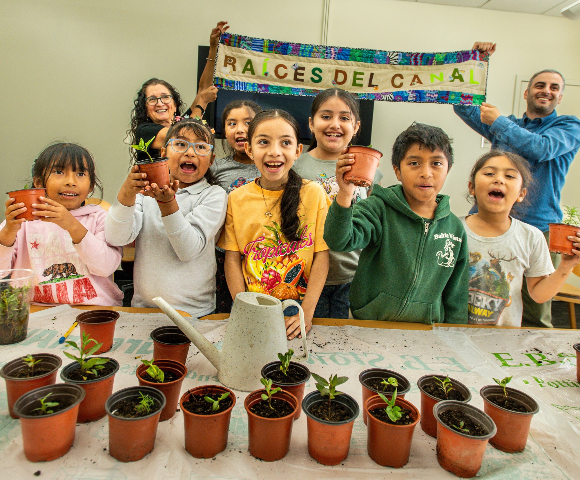 Raíces del Canal youth and community members proudly holding plants and their handmade banner